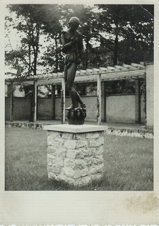 Zdjęcie o wysokości 14,4 cm i szerokość 10,0 cm, bok ząbkowany. Przedstawia rzeźbę Szczurołapa zlokalizowaną na Reitzensteinplatz (Plac Warszawski).